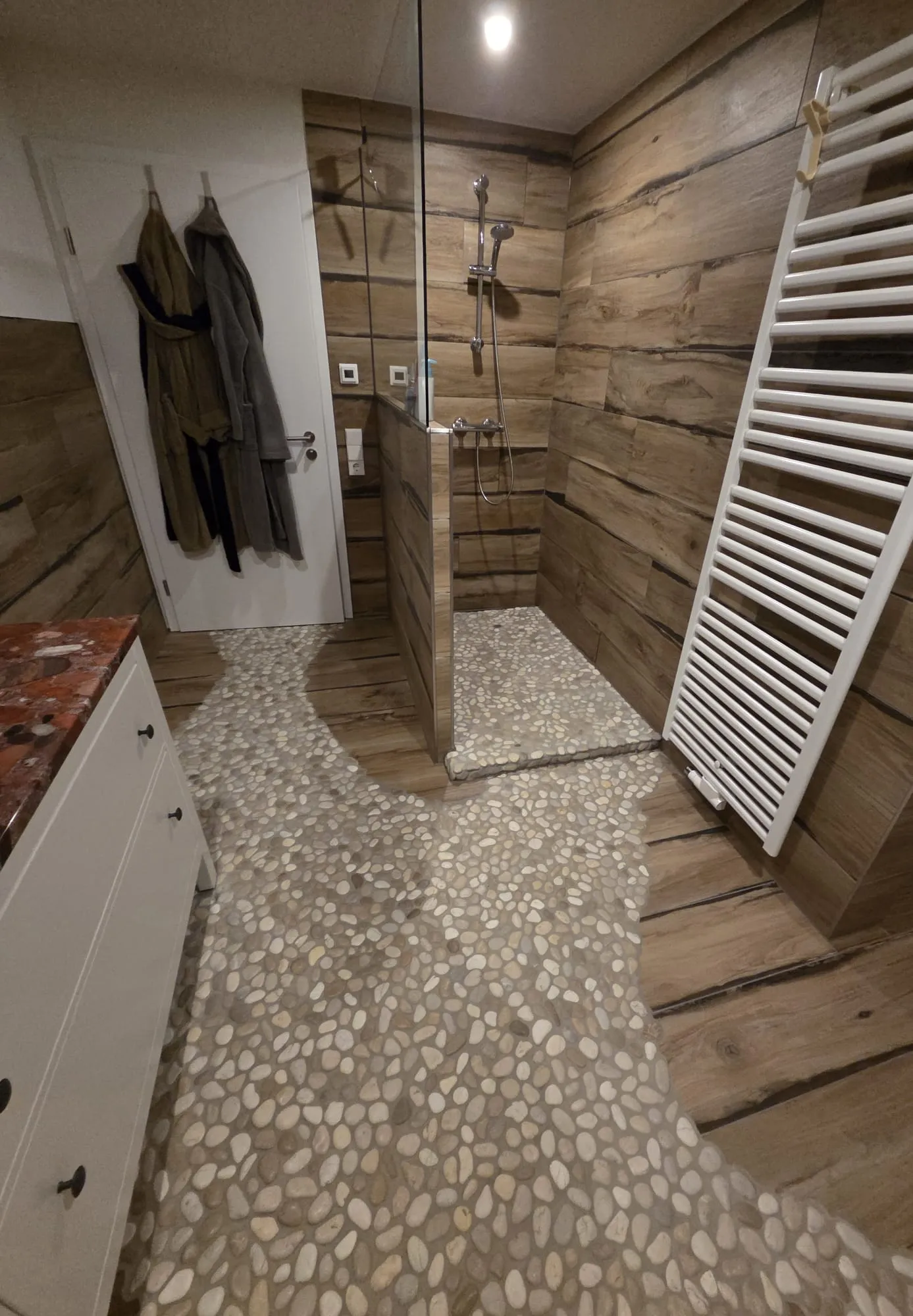 Bad mit Holzoptik-Wänden, Boden aus Flusskieseln und bodenebener Dusche